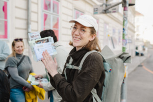 Christina Lengauer von der Programmleitung mit Print-Produkten und Rucksack bei einer Tour. 